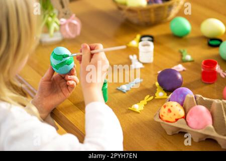 Le mani del bambino della lettera che dipinge le uova di Pasqua sul tavolo di legno. Preparazione per la celebrazione pasquale. Foto Stock