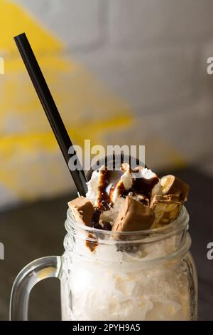 Freakshake in barattolo con paglia da cocktail, pezzi di cioccolato e biscotti, su un tavolo di legno scuro. Verticale Foto Stock