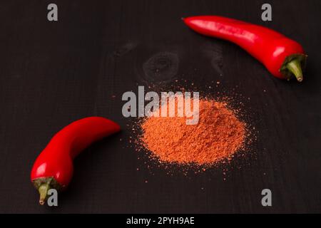 Due cialde di peperoni jalapeno rossi caldi e uno scivolo di pepe in polvere su una superficie di legno nero. Copia spazio Foto Stock