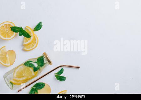Flacone in vetro con limonata con cannuccia metallica. Zenzero, limone, menta su superficie bianca. Base piatta, vista dall'alto. Copia spazio Foto Stock