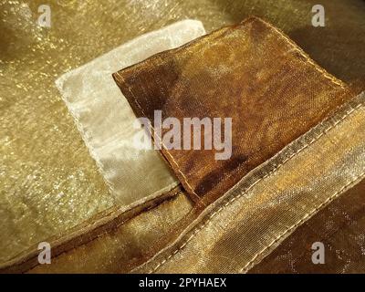 Anelli per tende. Splendido tessuto dorato. Organza nelle tonalità giallo, arancione, beige e marrone. Pieghe nel tessuto. Gradiente luminoso sotto la luce. Tulle di seta piegato. Materiale per tende trasparente Foto Stock