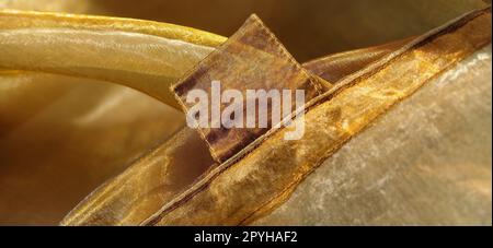 Anelli per tende. Splendido tessuto dorato. Organza nelle tonalità giallo, arancione, beige e marrone. Pieghe nel tessuto. Gradiente luminoso sotto la luce. Tulle di seta piegato. Materiale per tende trasparente Foto Stock