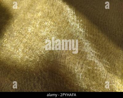 Splendido tessuto dorato. Organza nelle tonalità giallo, arancione, beige e marrone. Pieghe nel tessuto. Gradiente luminoso sotto la luce. Tulle di seta piegato. Materiale per tende trasparente Foto Stock