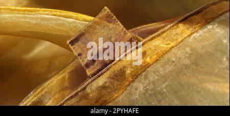 Anelli per tende. Splendido tessuto dorato. Organza nelle tonalità giallo, arancione, beige e marrone. Pieghe nel tessuto. Gradiente luminoso sotto la luce. Tulle di seta piegato. Materiale per tende trasparente Foto Stock