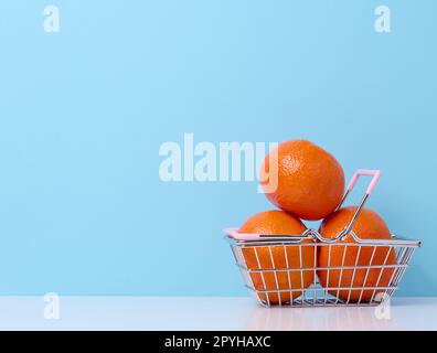 Mandarini maturi in un carrello di shopping in metallo in miniatura su uno sfondo blu, concetto di aumento del prezzo degli agrumi Foto Stock