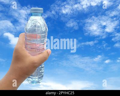 Mano dell'uomo che tiene una bottiglia di plastica di acqua e di fondo del cielo Foto Stock