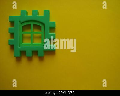 costruttore di bambini in plastica verde su sfondo giallo. Spazio di copia con vista dall'alto piatta. Sfondo di blocchi di plastica. Sviluppare giocattoli, gioco Foto Stock