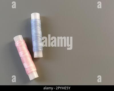 Bobine di filo rosa e blu su sfondo grigio. Industria tessile Foto Stock