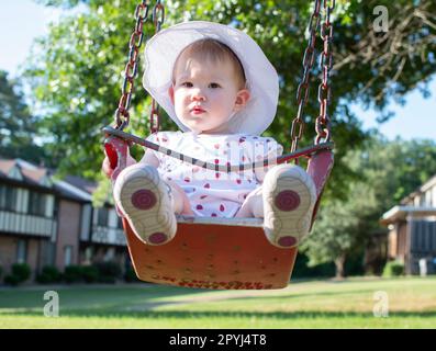 Bambina caucasica seduta in un altalena in una soleggiata giornata estiva Foto Stock