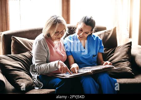 Portare la storia in vita. un'infermiera e una donna anziana che guardano insieme un album fotografico. Foto Stock