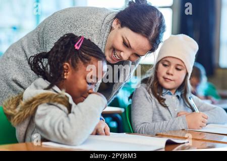 Dedicato ad aiutare i suoi studenti a capire il lavoro. le ragazze della scuola elementare ottengono l'aiuto dal loro insegnante nella classe. Foto Stock