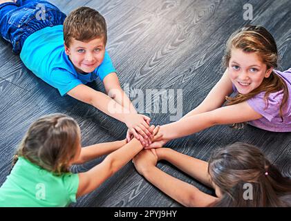 I nostri amici sono i migliori di sempre, mani giù. un gruppo diversificato di bambini che si trovano sul pavimento e che si uniscono le mani in solidarietà. Foto Stock