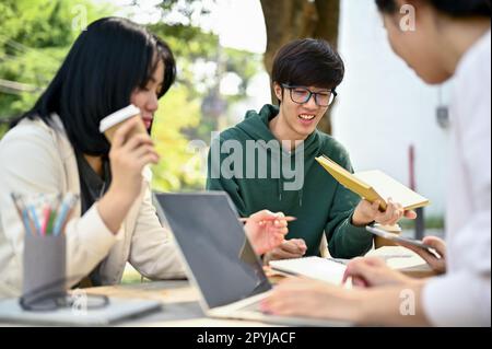 Nerd e giovane asiatico studente universitario maschile intelligente tutorando la matematica ai suoi amici, preparando per l'esame in un campus parco insieme. Foto Stock