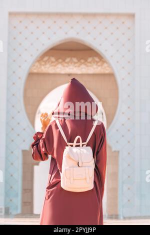 La grandezza della Grande Moschea dello Sceicco Zayed è amplificata dalla vista di una ragazza turistica di Abaya che vagabondeggia attraverso le sue sale. Foto Stock
