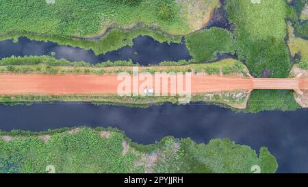 Veduta aerea verticale lungo la strada sterrata di Transpantaneira con una macchina e adiacenti lagune blu e prati verdi, Wetlands, Mato Grosso, Brasile Foto Stock