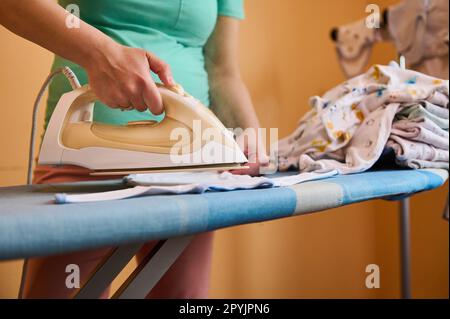 Ferro da stiro elettrico a vapore beige per primo piano in mano di una donna incinta, stiratura e stiratura a vapore di capi di lavanderia e di vestiario per neonati. Foto Stock