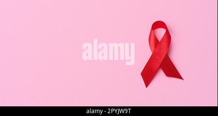 Un nastro rosso seta a forma di arco su sfondo rosa, simbolo della lotta contro l'AIDS e segno di solidarietà e sostegno Foto Stock