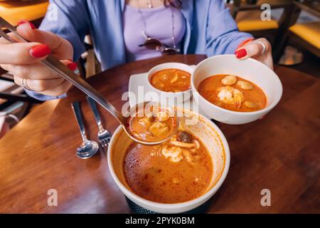 Versa la deliziosa e speziata zuppa tradizionale tailandese Tom Yam con pesce sui piatti del ristorante Foto Stock