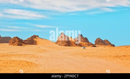 Tipico paesaggio desertico ad Alula, Arabia Saudita, sabbia con alcune montagne, piccolo veicolo fuoristrada, uomo locale e cammelli a distanza Foto Stock