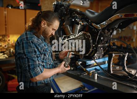 Biker riparatore che guarda il ricambio nel suo e mentre lavora in garage Foto Stock