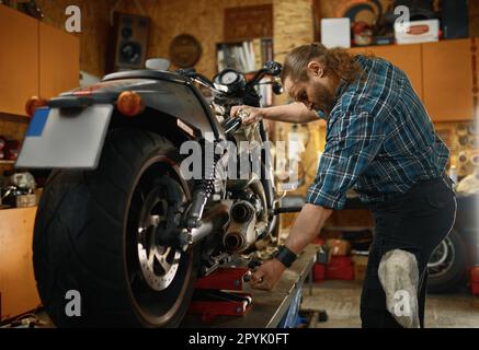 Meccanico moto che lavora con cacciavite riparando moto in garage Foto Stock