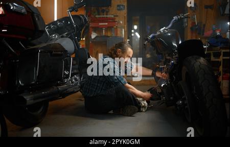 Uomo maturo biker riparazione moto in garage di sera Foto Stock