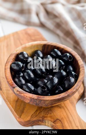 Olive nere snocciolate in una ciotola di legno sul tavolo da cucina. Foto Stock