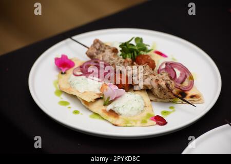 souvlaki con pita e salsa tzatziki su un piatto bianco Foto Stock