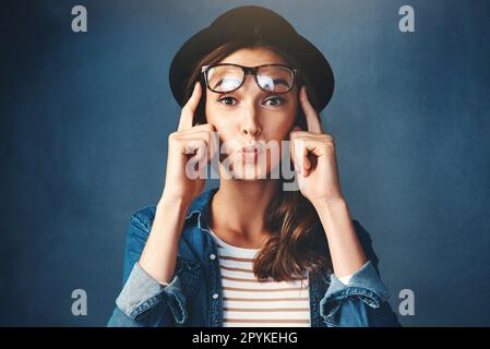 I miei occhi mi ingannano. Studio shot di una giovane donna attraente sollevando i suoi occhiali e poouting su uno sfondo blu. Foto Stock