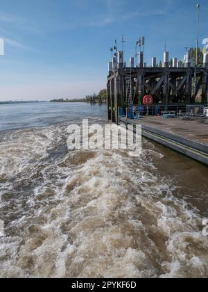 Acqua vorticosa da una barca in partenza su un fiume con il molo sullo sfondo Foto Stock