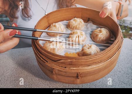 Ragazza con bacchette che prova deliziosa, prelibatezza tradizionale cinese, gnocchi Xiaolongbao, o baozi buns presentato in un piatto di bambù per un autentico Foto Stock