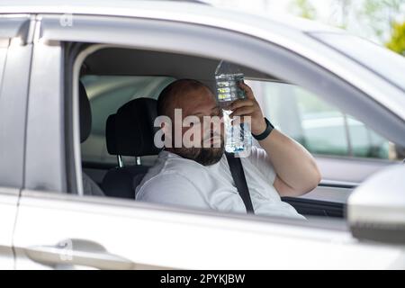 L'uomo stanco e sovrappeso guida l'auto con aria condizionata rotta in estate caldo tempo. Foto Stock