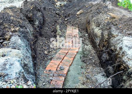 Posa e reinserimento di un frammento di una linea di cavi sotterranei di bassa profondità e messa a fuoco selettiva Foto Stock