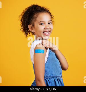 Felice, ritratto e bambino con un intonaco in uno studio per una ferita, ferita o ferita sul suo braccio. Felicità, sorriso e modello sano di bambina in posa con un Foto Stock