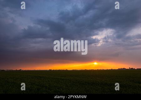 Il sole tramonta sulle pianure sotto un cielo tempestoso Foto Stock