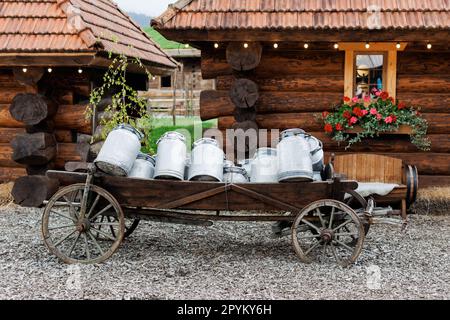 Vecchio carrello in legno con un sacco di barattoli in alluminio utilizzato una volta molto tempo fa dal contadino per consegnare i prodotti vicino a case in legno in paese... Foto Stock