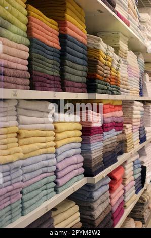 Nuovi asciugamani in spugna colorati impilati su uno scaffale in un negozio di tessuti Foto Stock