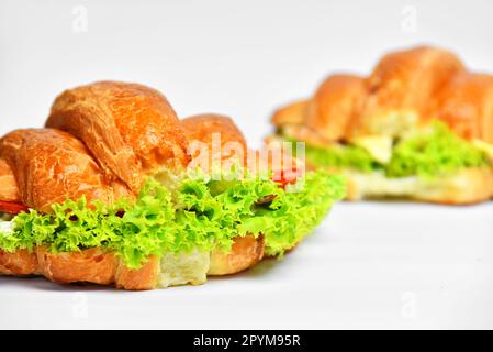 Croccante panino di croissant fresco con lattuga su sfondo bianco. Foto Stock