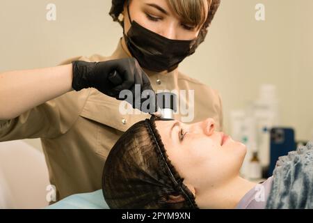 Il medico dermatologo esamina i moli e i segni di nascita della paziente femminile in clinica. Medico che usa il dispositivo di dermoscopia durante il controllo della pelle della donna del cliente. Prevenire Foto Stock