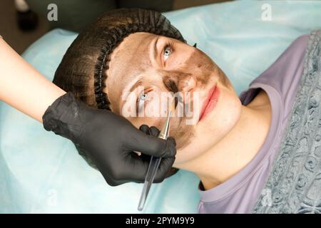 Il cosmetologo applica il nanoogel di carbonio del volto del cliente. Preparazione per il trattamento laser della pelle. Pelatura del viso in carbonio. Cosmetologia hardware Foto Stock