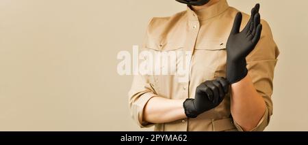 Irriconoscibile medico cosmetologo femminile in uniforme mette su guanti neri. Concept procedura sicura e sterile in salone di bellezza o clinica cosmetica Foto Stock