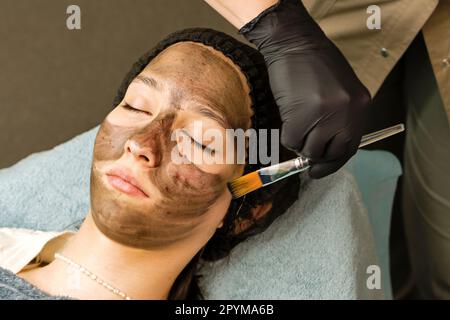 Сosmetician applica il nanogel di carbonio del volto del cliente. Preparazione per il trattamento laser della pelle. Pelatura del viso in carbonio. Cosmetologia hardware. Scienza della pelle Foto Stock