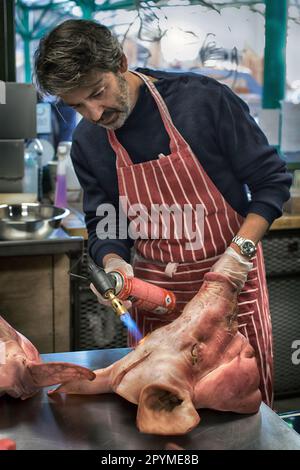 L'uomo che brucia i capelli grossolani della porchetta al maiale in un giorno, un giorno di corso di macelleria Foto Stock