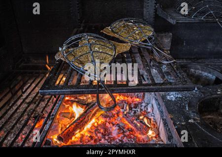 Cucinare il pesce in gabbie di ferro sopra fuoco di legno al ristorante Brat a Londra, Regno Unito Foto Stock