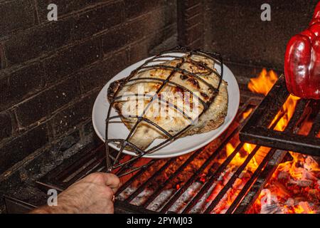 Cucinare il pesce in gabbie di ferro sopra fuoco di legno al ristorante Brat a Londra, Regno Unito Foto Stock