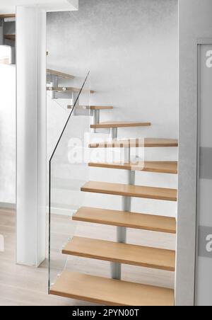 Scala con scale in legno e ringhiere in vetro nel moderno interno di un appartamento, casa. Scala di design in un appartamento su due livelli, vetro smerigliato Foto Stock