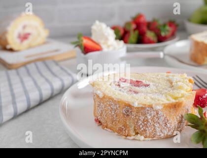 Fetta di swiss roll con panna montata e ripieno di fragole su un piatto su sfondo chiaro Foto Stock