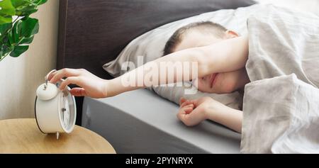 ragazzo sdraiato sul letto e la sveglia di mattina. la mano dei bambini arriva per la sveglia Foto Stock