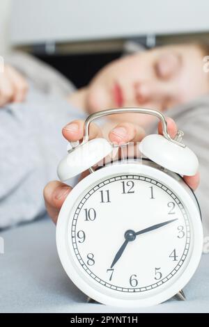 ragazzo sdraiato sul letto e la sveglia di mattina. la mano dei bambini arriva per la sveglia Foto Stock