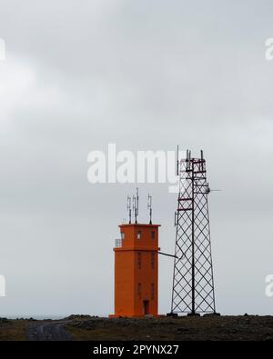 Una torre faro arancione accanto ad una torre radiofonica metallica, Hvalnes, Islanda. Foto Stock